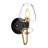 Introducing the Armand 1 Light Wall Light, featuring a sleek wall-mounted design with a charcoal black circular base and aged brass plated accents. Its clear teardrop-shaped glass shade houses an exposed filament bulb, blending contemporary style with vintage elegance.