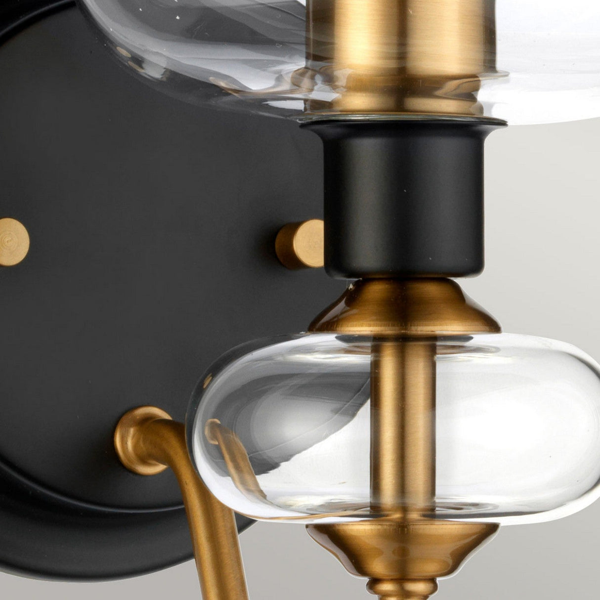 Close-up of the Armand 1 Light Wall Light, showcasing a clear glass orb and a sophisticated aged brass plated and charcoal black paint design. The fixture combines smooth, rounded shapes with charcoal black accents for an elegant appearance.