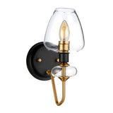 The Armand 1 Light Wall Light combines a stylish design with its clear glass shade and exposed filament bulb. It features aged brass plating along with charcoal black paint, mounted on a circular black base and supported by a curved gold accent, enhancing the sophistication of any room.