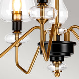 A close-up of the Armand 5 Light Chandelier - Aged Brass Plated & Charcoal Black Paint highlights its clear glass bulbs and elegant black and aged brass accents, set against a gray background.