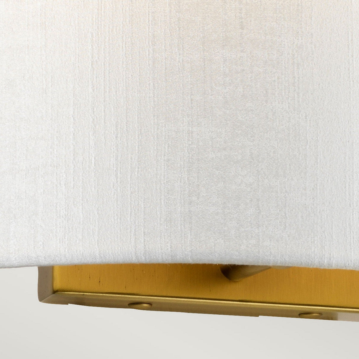 Close-up of the textured faux silk shade with a glimpse of the aged brass base beneath. The background is a neutral, soft beige, elegantly framing this Cooper Medium Curved Wall Light.
