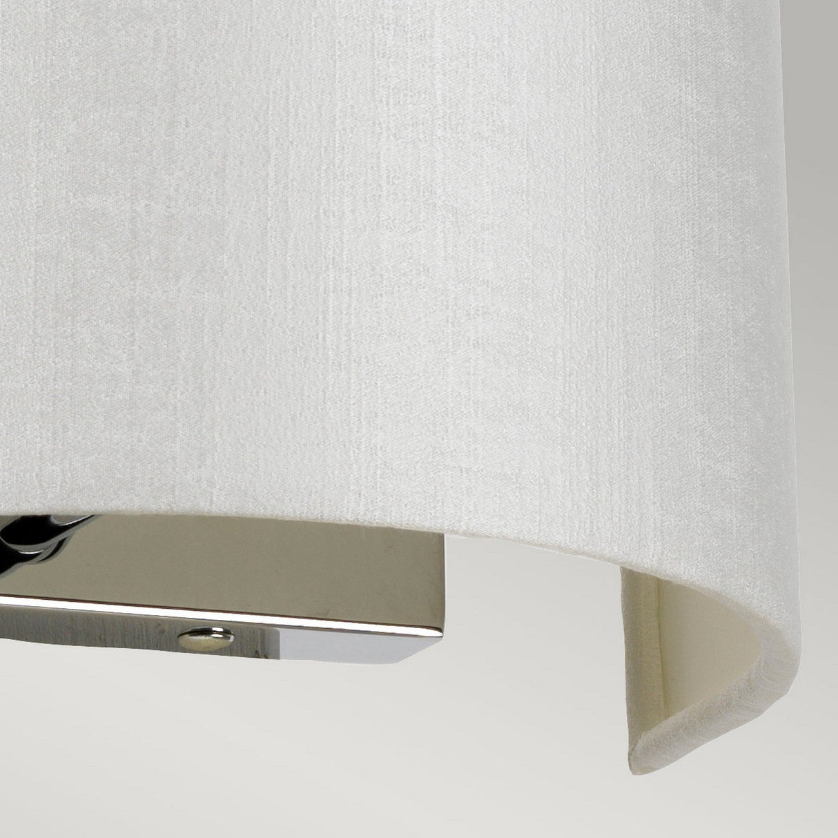 A close-up of the Cooper Small Curved Wall Light reveals a textured white lampshade elegantly paired with a polished chrome base. The concealed light source emits a soft, diffused glow against the neutral gray background.