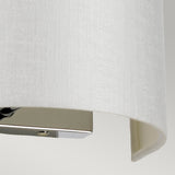 A close-up of the Cooper Small Curved Wall Light reveals a textured white lampshade elegantly paired with a polished chrome base. The concealed light source emits a soft, diffused glow against the neutral gray background.