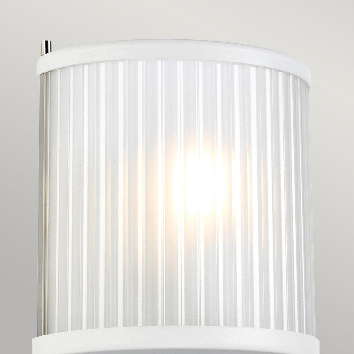 The Corona Wall Light - White is a cylindrical wall sconce with a ribbed texture that casts a warm glow. It features white trim at both the top and bottom, along with a metal fixture at the top edge. The minimalist design enhances its modern appeal against the neutral wall background.