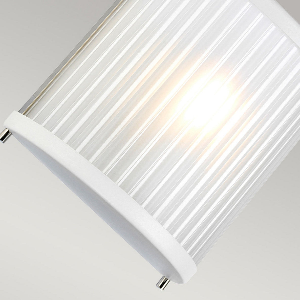 Close-up of a Corona Wall Light - White, featuring a ribbed glass shade. The light emanates a warm, soft glow, accentuating its sleek cylindrical design and modern charm. A pale gray background complements its minimalist aesthetic.