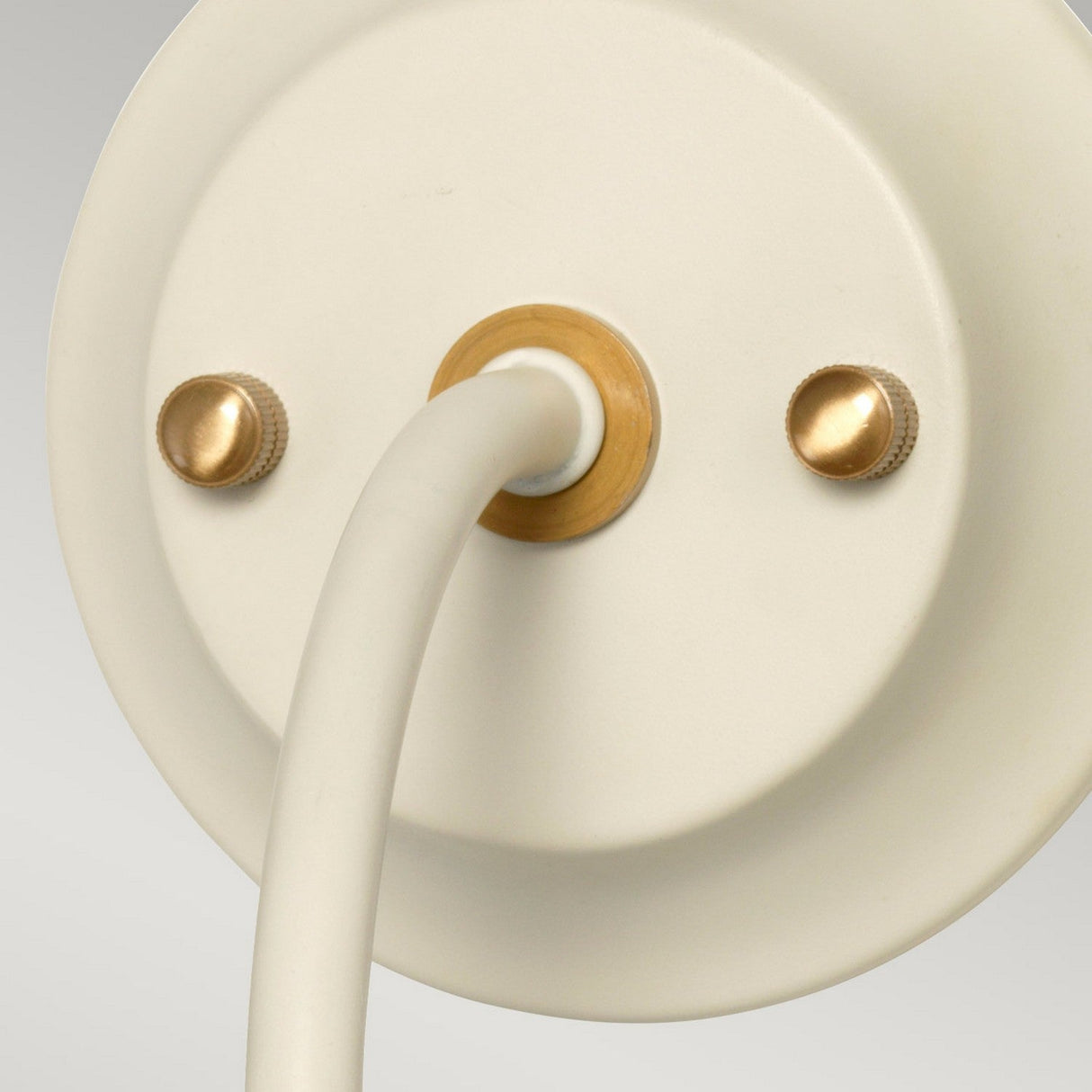 Close-up of the Cosmos Wall Light in cream painted finish and aged brass accents, showcasing its round shape with a cylindrical attachment and two small gold screws for fastening. The ambient lighting design is minimalistic and modern, bringing a touch of retro elegance to any space.