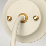 Close-up of the Cosmos Wall Light in cream painted finish and aged brass accents, showcasing its round shape with a cylindrical attachment and two small gold screws for fastening. The ambient lighting design is minimalistic and modern, bringing a touch of retro elegance to any space.