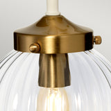 A close-up of a pendant light featuring a ribbed glass shade and a brass fixture, evoking retro design elements. A glowing bulb creates a warm, ambient light effect, reminiscent of the Cosmos Wall Light - Cream Painted & Aged Brass with its two decorative bolts on either side.