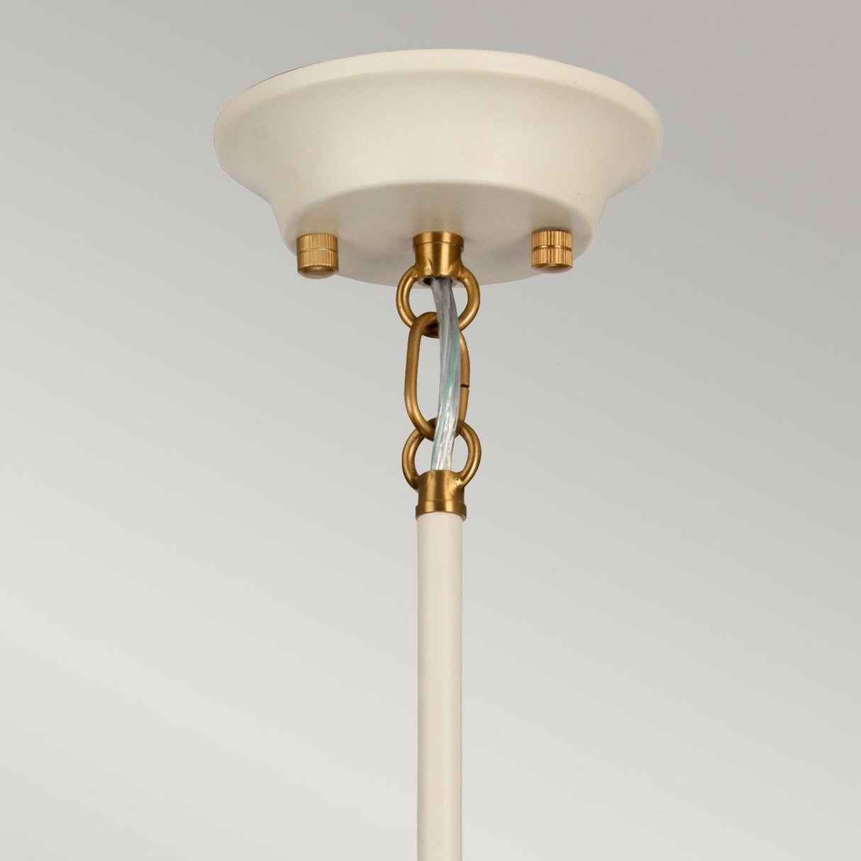 A cream-painted ceiling mount with a beige rod descends, connected by aged brass chain links to the fixture. The Cosmos 9 Light Pendant - Cream Painted & Aged Brass introduces a light blue hue that contrasts with the mount and links. Its presence is further accentuated against the plain light gray background, creating an elegant centerpiece.