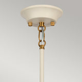 A cream-painted ceiling mount with a beige rod descends, connected by aged brass chain links to the fixture. The Cosmos 9 Light Pendant - Cream Painted & Aged Brass introduces a light blue hue that contrasts with the mount and links. Its presence is further accentuated against the plain light gray background, creating an elegant centerpiece.