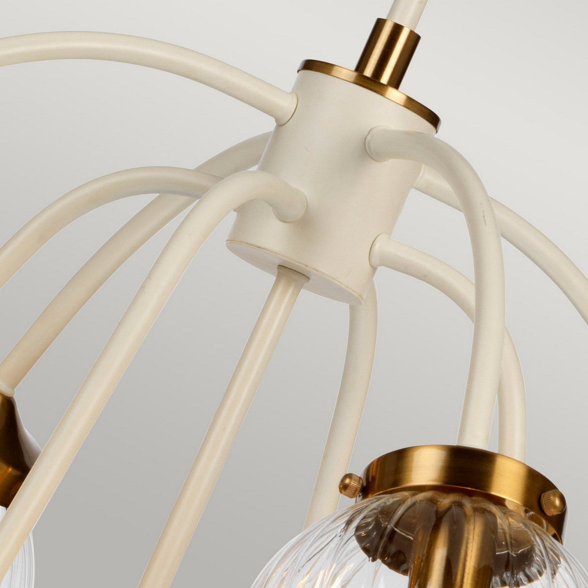 Detailed view of the Cosmos 9 Light Pendant in cream painted and aged brass. This fixture showcases elegantly arched metal rods complemented by hand-blown glass shades featuring ribbed patterns, offering a modern and sophisticated aesthetic.