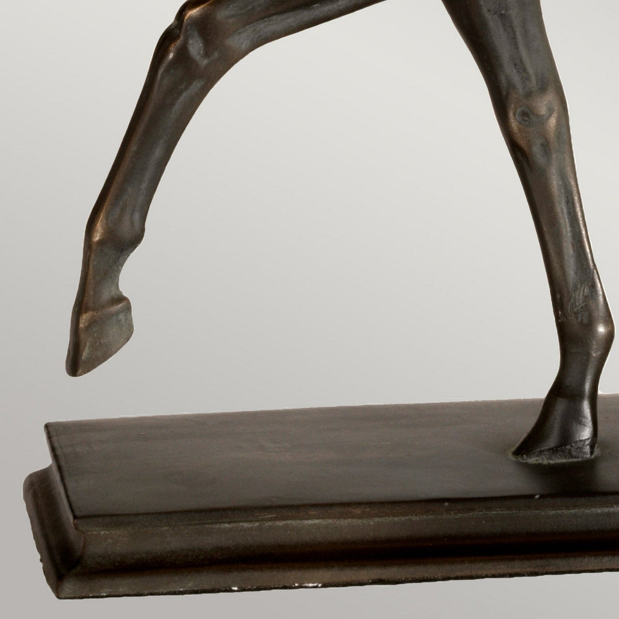 A close-up of a bronze horse statuette highlights two legs in a dynamic pose, accentuating the detailed muscular structure and rich bronze patina. Reminiscent of the Dorado Table Lamp with Rectangle Shade in Bronze Patina, the sculpture is mounted on a rectangular base.