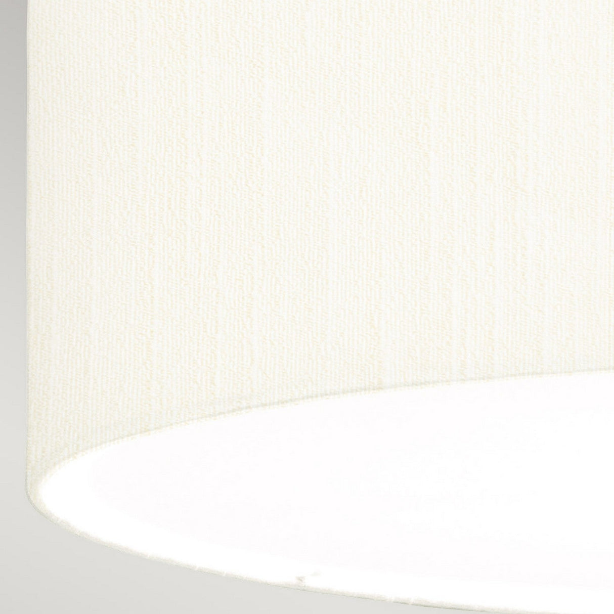 A close-up of the ivory shade from the Fletcher 26" Flush - Aged Brass fixture highlights its faux silk texture, featuring a subtle gradient from cream to bright white that showcases the fabric's weave pattern. The slightly curved bottom edge is set against a neutral gray background, adding a touch of elegance to any room when paired with the aged brass finish.