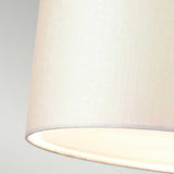 Close-up of an ivory fabric lampshade emitting a soft, warm light set against a light gray background, reminiscent of the elegant Fletcher 34" Flush - Aged Brass with Ivory Shade. The texture of the fabric appears smooth and slightly woven, complementing the aged brass ceiling fixture beautifully.