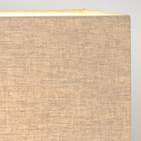 A close-up of the bronze patina Halkirk Table Lamp with its beige hessian rectangle shade glowing warmly, set against a neutral background. The visible texture of the woven fabric adds a soft, cozy feel to the image.