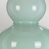 A detailed view of the Harbin Gourd Table Lamp with Tall Empire Shade showcases its smooth, glossy, pastel green surface and distinctive two-tiered shape reminiscent of a gourd. The celadon finish beautifully reflects light, producing bright highlights against the simple light gray background.