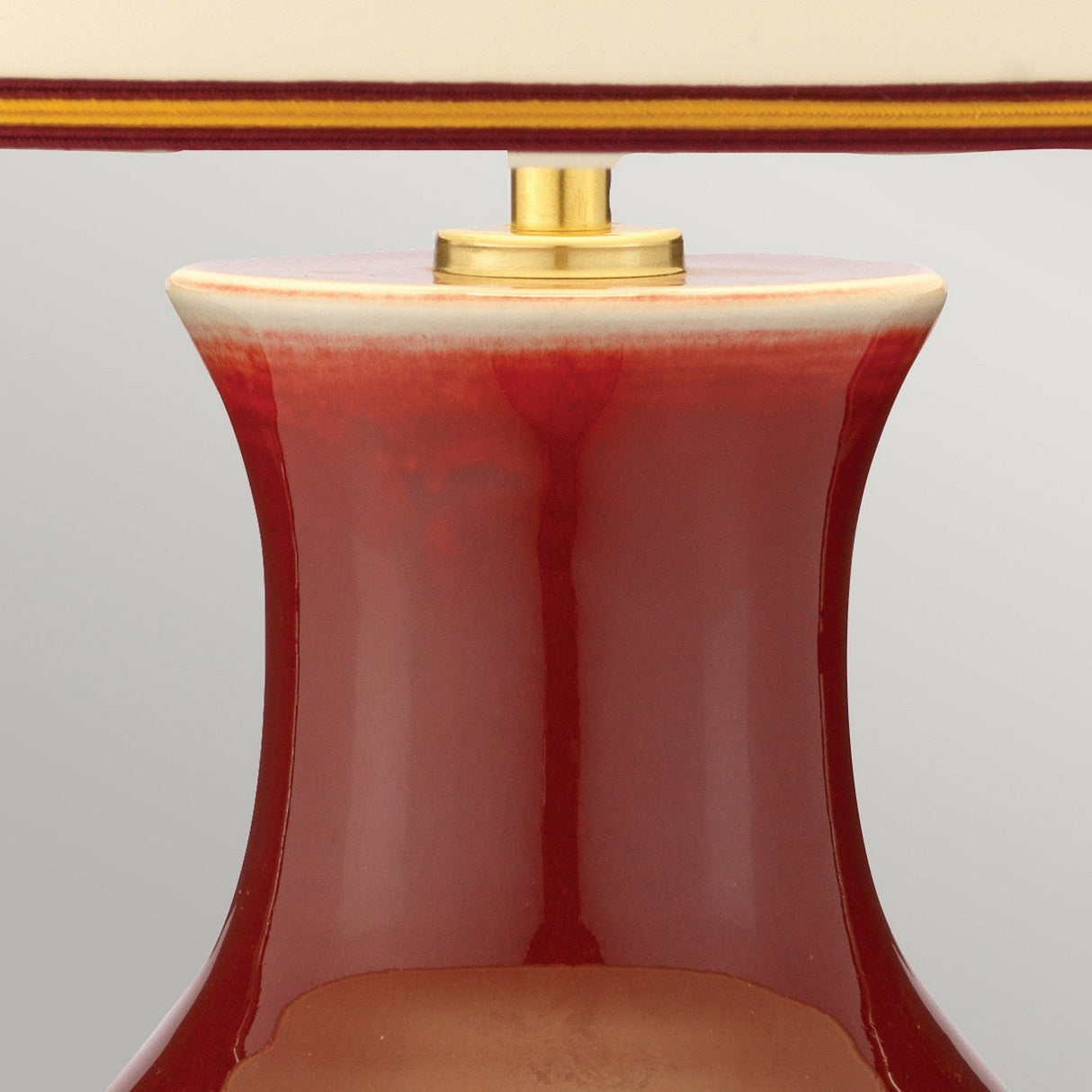 Close-up of the Majin 1 Light Table Lamp's base, featuring an elegant design with a glossy oxblood red porcelain vase shape and a golden rod extending upward. The top is adorned with a cream cap and a red stripe rim, while the reflection highlights the lamp's smooth surface texture.