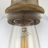 Close-up of an Edison-style light bulb with a visible filament, encased in a clear glass cover, and mounted in the Matrimonio 1 Light Mini Pendant fixture, featuring textured driftwood and dark weathered zinc for a charming rustic lighting effect.
