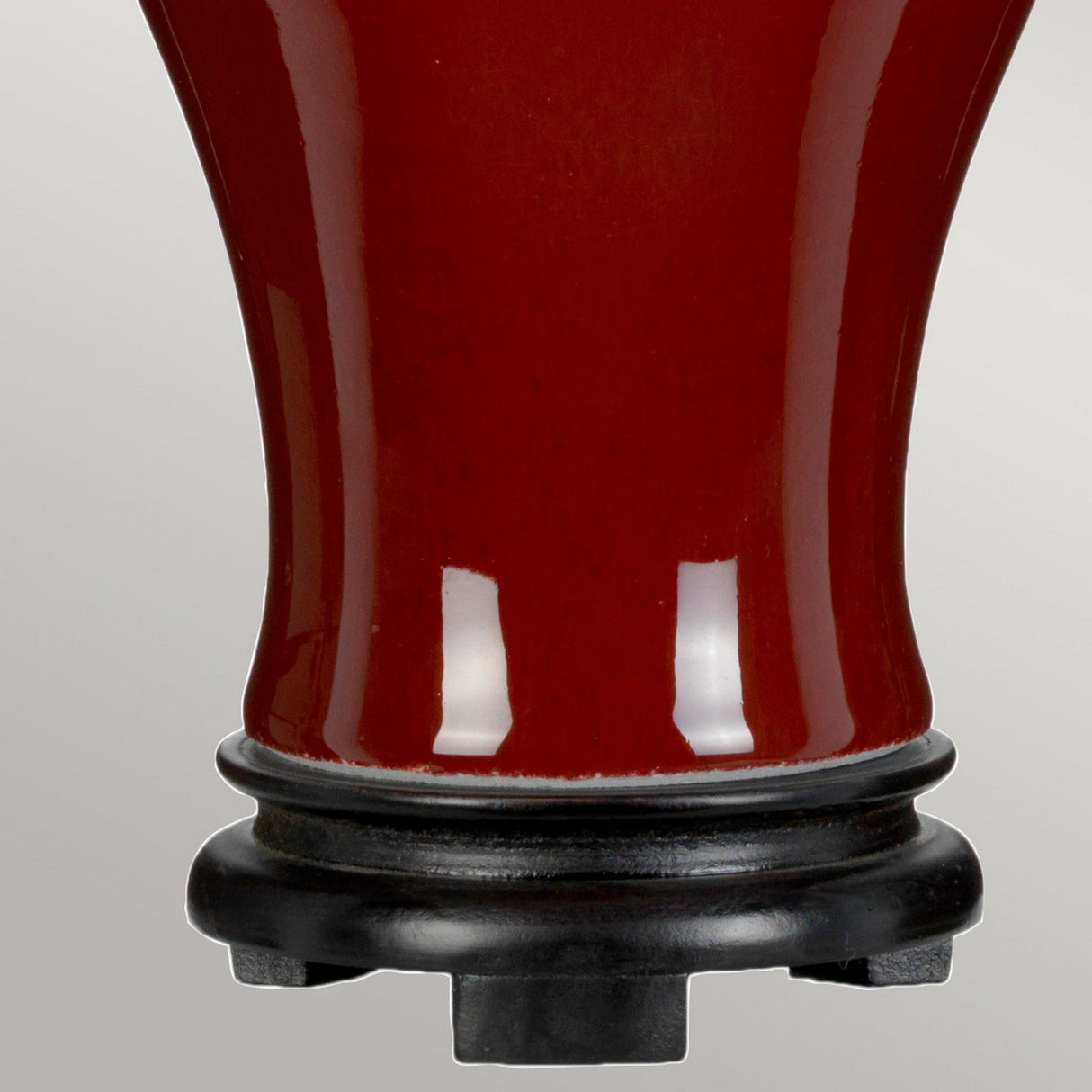 A close-up image features the base of an Oxblood Temple Jar Table Lamp with Tall Empire Shade, highlighting its glossy finish and oriental elegance. It sits atop a black stand against a neutral backdrop.