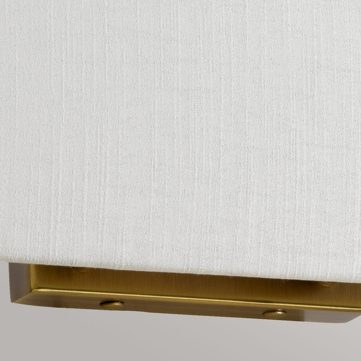 Close-up of the edge of an ivory-textured lampshade belonging to the Riley Large Rectangular Wall Light in aged brass. The background is gray, offering a subtle contrast.