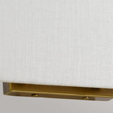 Close-up of the edge of an ivory-textured lampshade belonging to the Riley Large Rectangular Wall Light in aged brass. The background is gray, offering a subtle contrast.