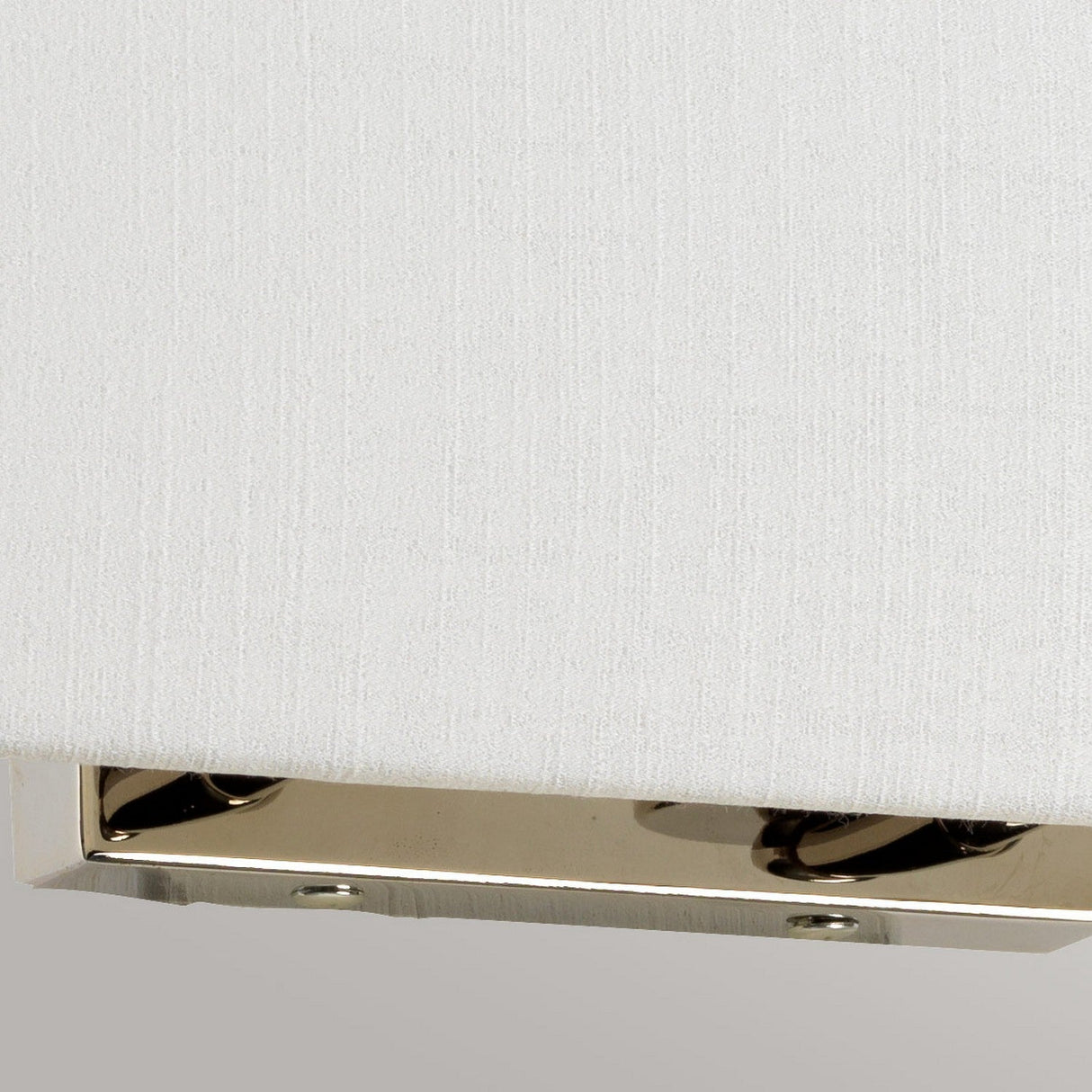 A close-up of the corner of the Riley Large Rectangular Wall Light in polished chrome against a textured white background showcases its shiny metal surface. The reflected light forms a subtle pattern, capturing the essence of contemporary design lighting.