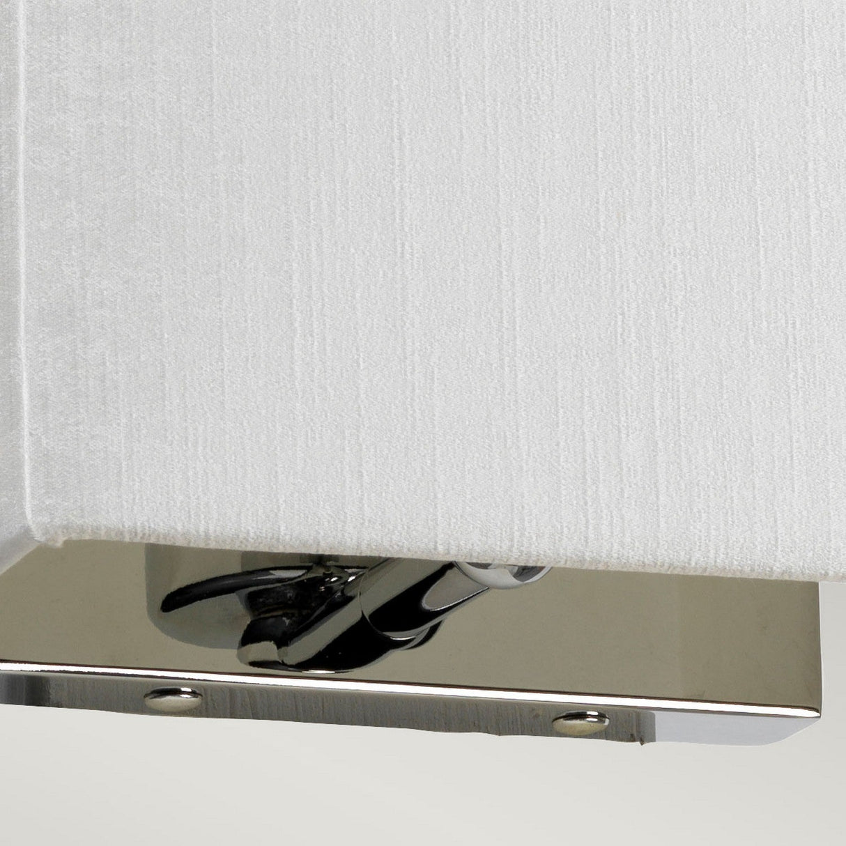 A close-up of the Riley Small Rectangular Wall Light - Polished Chrome showcases its contemporary lighting design, featuring a white fabric shade and a polished chrome base that exudes modern elegance.