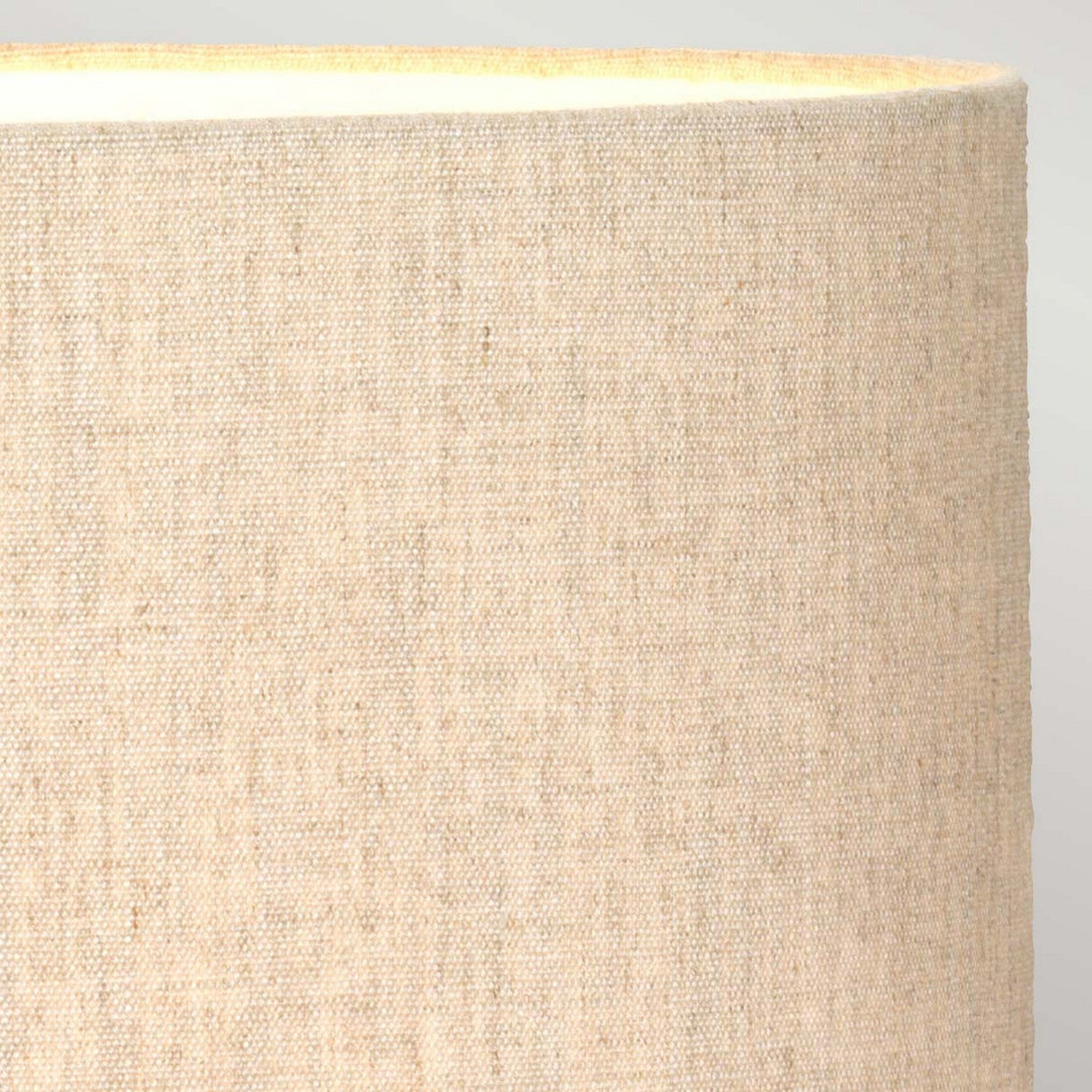 Close-up of the top section of a beige, textured fabric lampshade on the Rufus Table Lamp With Oval Shade - Bronze Patina. The woven pattern displays subtle variations in tone, with lighting that accentuates its texture through a soft glow at the top edge. The entire setup exudes an elegant charm against a neutral background.