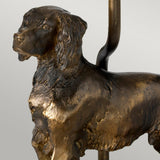 The Rufus Table Lamp with Oval Shade features a bronze patina reminiscent of a finely detailed dog sculpture, capturing an alert expression and intricate fur texture. The lamp showcases the craftsmanship similar to a statuette, with its head slightly turned to emphasize its exquisite finish. Its simple backdrop enhances the artistry and structure of this piece.