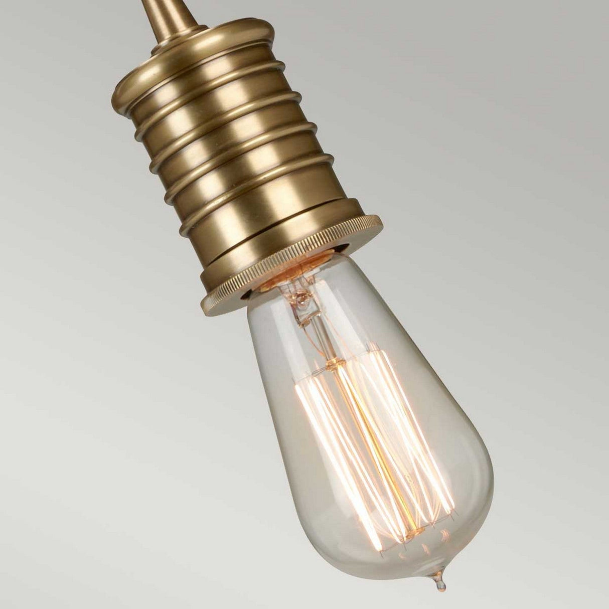 A close-up of the Douille 1 Light Pendant in an aged brass finish, featuring a lit LED filament lamp that highlights its warm glow and intricate filaments against a neutral background.