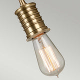 A close-up of the Douille 1 Light Pendant in an aged brass finish, featuring a lit LED filament lamp that highlights its warm glow and intricate filaments against a neutral background.