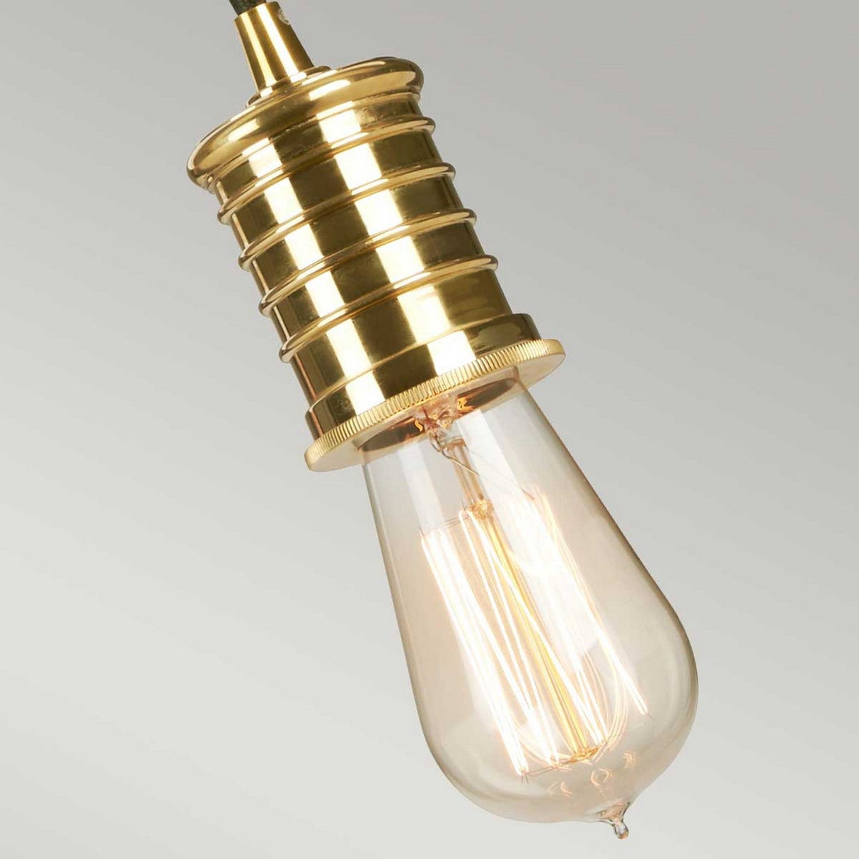 Close-up of the Douille 1 Light Pendant featuring a vintage-style LED filament bulb and a polished brass lamp holder. The elongated bulb emits a warm glow, accentuating its intricate filament against a plain background.