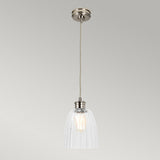 The Douille 1 Light Pendant in polished nickel features a vintage-style industrial design with a clear ribbed glass shade hanging from a twisted cord. The LED filament bulb inside provides a warm glow, perfectly complemented by the fixture's polished nickel base against a light gray background.