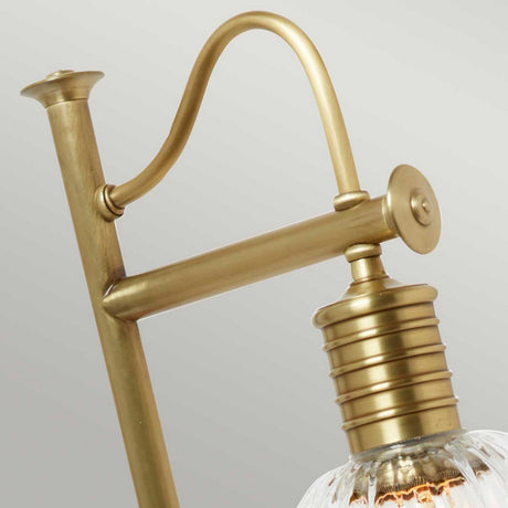 Detailed view of the Douille Table Lamp in aged brass, featuring a curved arm and ribbed socket. This vintage lighting piece showcases a clear glass shade and exposed bulb, embodying an industrial aesthetic against a neutral background.