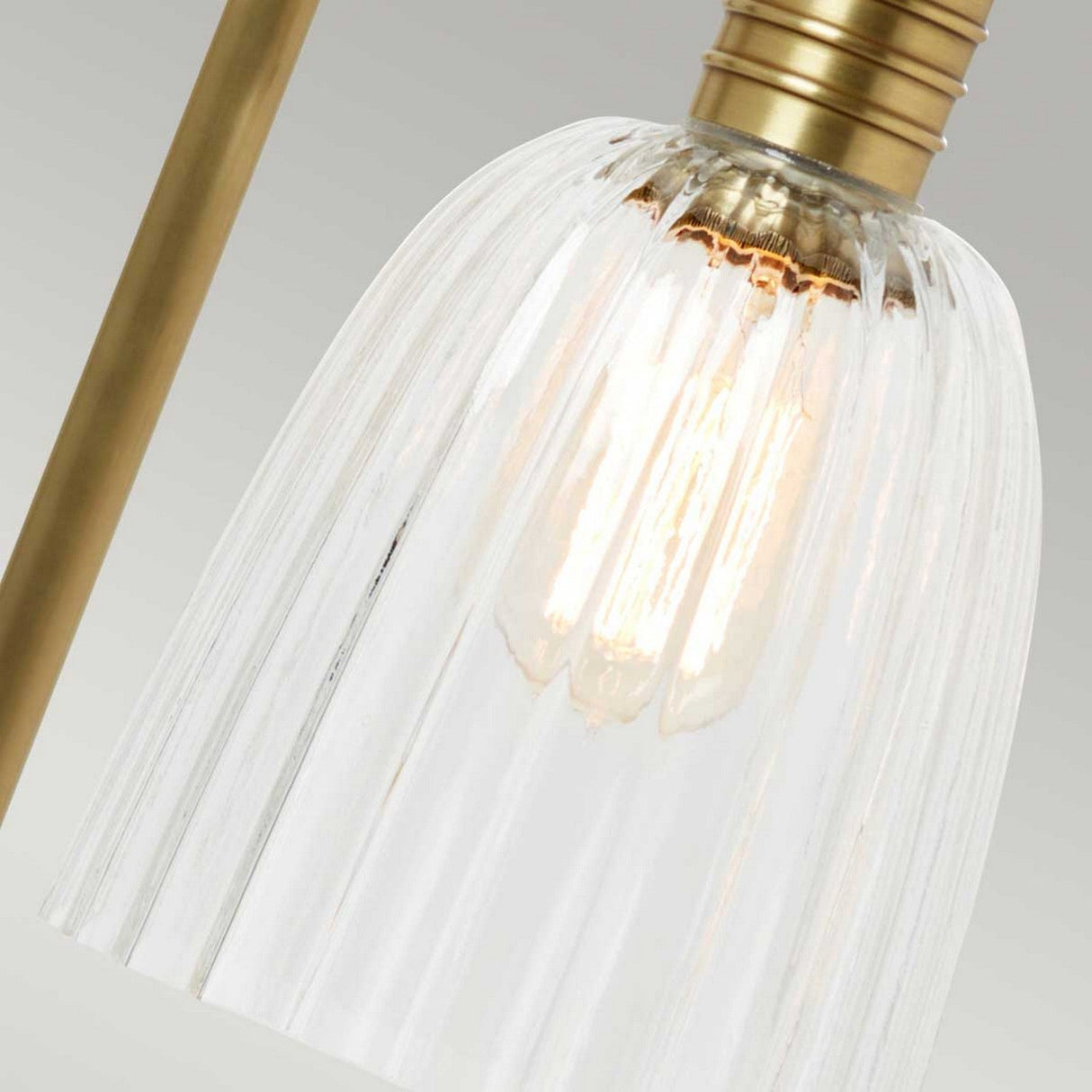 Close-up of a lit bulb inside a glass lampshade with vertical grooves. The Douille Table Lamp in aged brass provides a warm and elegant appearance. Its vintage lighting style casts a soft glow through the textured glass, enhancing the industrial aesthetic of any space.