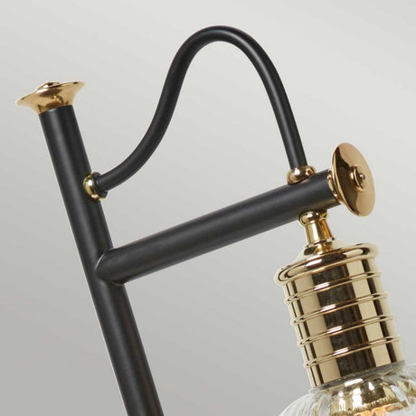 Close-up of the Douille Table Lamp - Black & Polished Brass, showcasing its sleek black metal frame with polished brass accents. The cylindrical shape, decorative elements, and uniquely curved support provide a modern twist on vintage design, seamlessly blending industrial and contemporary styles.