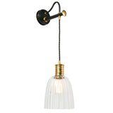 The Douille Wall Light features a vintage-style design with a wall-mounted pendant that includes a black metal arm and a polished brass finish, complemented by a clear ribbed glass shade. The visible bulb casts a warm glow, enhancing its classic and elegant appeal.