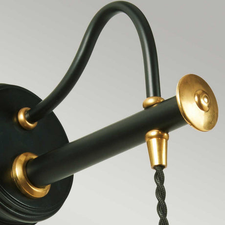 A close-up of the Douille Wall Light - Black & Polished Brass reveals its vintage-style lamp fixture, complete with a polished brass finish. It showcases a curved black arm, a round gold-toned end cap, and an elegantly hanging black fabric-covered cord against a light gray background.