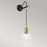 The Douille Wall Light in Black & Polished Brass is a vintage-style wall-mounted lamp featuring a transparent glass shade and an exposed bulb. This industrial wall light showcases a twisted black cord and a polished brass finish, all set against a neutral gray background.