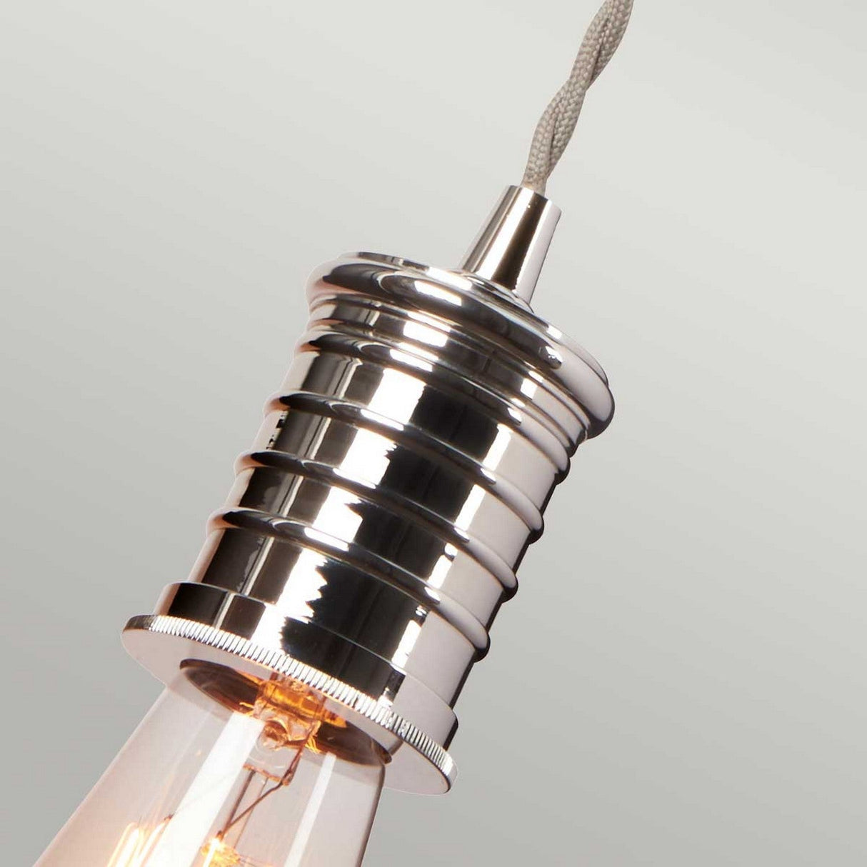 Close-up of the Douille Wall Light in polished nickel, showcasing a modern ribbed design with vintage-style LED filament lamps. This fixture is suspended from a braided cord, radiating an industrial style with vintage-inspired charm against a simple, neutral background.