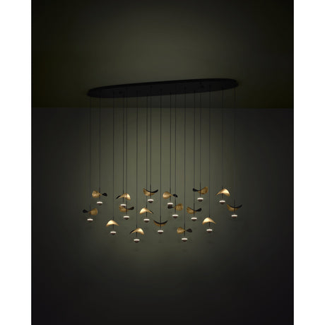 Dracera 17 Light Linear Pendant Light in black steel, with an oval ceiling canopy, fine black cords, and curved leaf-shaped shades in black and gold catching warm LED glow.