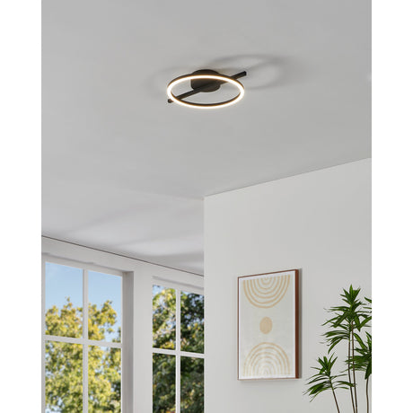 Dralena LED flush ceiling light with a slim black ring and crossbar design, illuminated in warm white, mounted on a white ceiling in a living room setting.