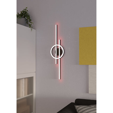 Dralena black LED wall light with two offset vertical bars and a central ring, white diffuser lighting with red RGB backlight, shown on a grey wall in a living room setting.