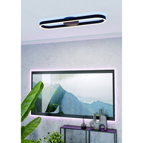 Dralena oval LED flush ceiling light in black, slim rounded aluminium and steel loop with round centre canopy, mounted on a grey living room ceiling above a wall-mounted TV.