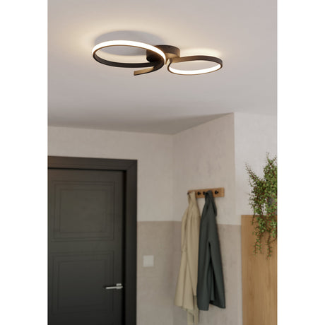 Drelvanne LED flush ceiling light in black with interlaced looped ribbons and white diffusers, shown illuminated on a hallway ceiling near a dark door and coat hooks.