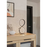 Drelvanne LED Table Lamp in black, a figure-of-eight shaped aluminium and steel design with a glowing white band, shown lit on a wooden sideboard beside a vase and framed art.