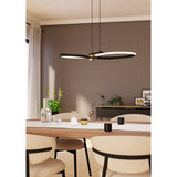 Drelvanne black pendant light with two looping LED bands crossing at a slim bar, hung above a dining table in a warm-toned dining room.