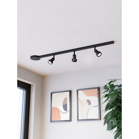 Easyt Set 3 Spots black track lighting kit with slim ceiling bar, oval canopy, and three adjustable GU10 spotlight heads, shown fitted above a room with framed wall art.
