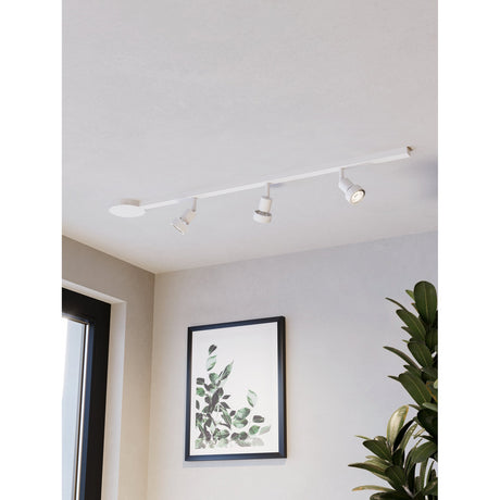 Easyt Set 3 Spots white track lighting kit mounted on a ceiling, a slim straight track with round canopy and three independently angled spotlights, shown above a framed leaf print and plant.