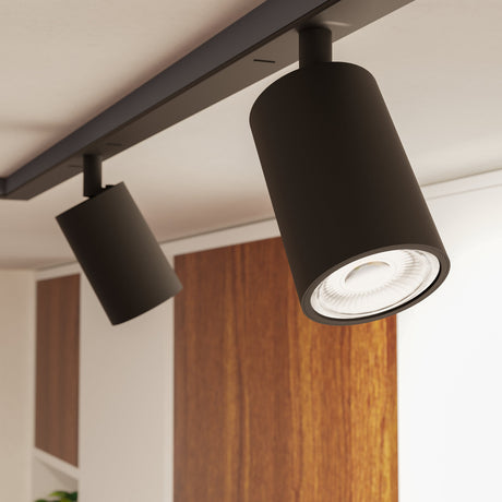 Easyt Spot Tube track spotlights in black plastic with cylindrical bodies and GU10 bulbs, mounted on a black ceiling track above a wood-panelled interior.